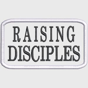 Peut inclure: Écusson brodé avec l'inscription "RAISING DISCIPLES" en lettres noires. Le texte est centré sur un fond rectangulaire blanc, bordé d'une couture blanche. Conçu pour être appliqué sur des vêtements ou des accessoires.