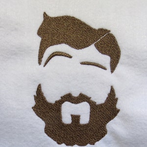 May include: Embroidered design of a person with a beard and mustache. The design is brown on a white background.