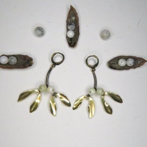 May include: A pair of gold earrings with white beads and gold leaf accents. The earrings are hanging from a hoop and have a delicate, organic design.