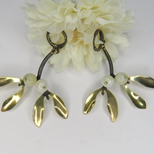 May include: A pair of gold mistletoe earrings with white pearl-like beads. The earrings are shaped like a branch with three leaves on each side.