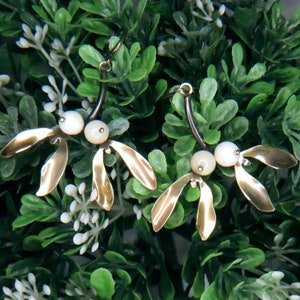 May include: A pair of gold-toned earrings with a delicate, leaf-like design and white pearl accents.
