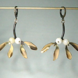 May include: A pair of gold mistletoe earrings with white pearl accents. The earrings are suspended from black metal hooks.