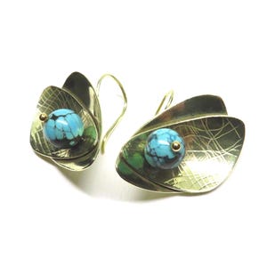 Peut inclure: Paire de boucles d'oreilles artisanales en métal doré en forme de feuilles. Chaque boucle d'oreille contient une perle turquoise avec un accent doré. Les boucles d'oreilles ont une fermeture à crochet, sur fond blanc.