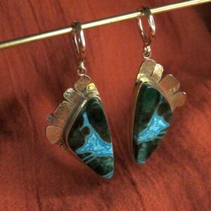 May include: A pair of dangle earrings featuring triangular stones with dark green and bright turquoise veined patterns. The stones are set in silver-toned metal with a textured, fan-like edge detail and secure hinged hoop closures at the top.