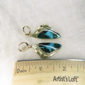 May include: A pair of gold-tone earrings featuring triangular inlays with black and turquoise marbled patterns. The earrings are positioned above a wooden ruler, showing each piece measures approximately 1.25 inches in total length.