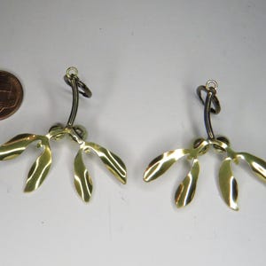 May include: A pair of gold-colored earrings shaped like mistletoe sprigs with black metal hooks.