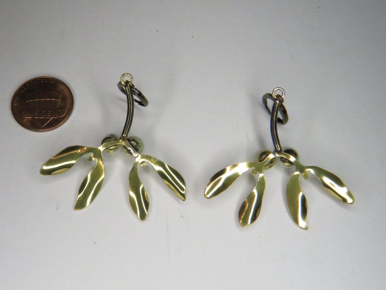 May include: A pair of gold-colored earrings shaped like mistletoe sprigs with black metal hooks.