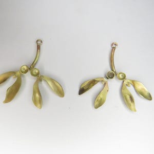 May include: Two gold-toned metal earrings shaped like maple tree seeds with three lobes each. The earrings are attached to a curved wire.