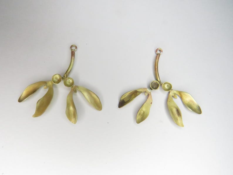 May include: Two gold-toned metal earrings shaped like maple tree seeds with three lobes each. The earrings are attached to a curved wire.