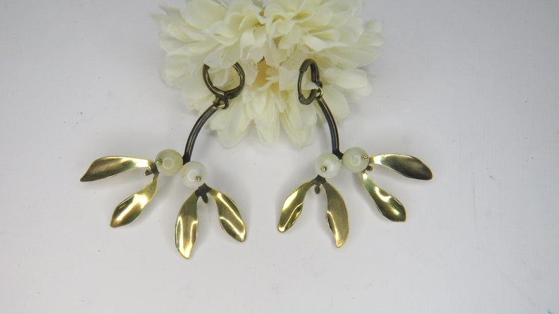 May include: A pair of gold mistletoe earrings with white pearl-like beads. The earrings are shaped like a branch with three leaves on each side.