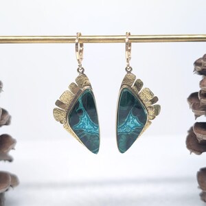 May include: A pair of drop earrings featuring triangular-shaped stones with deep green and bright turquoise marbled patterns. The stones are set in textured gold-tone metal frames with a fan-like edge and attached to small gold-tone hoop clasps.