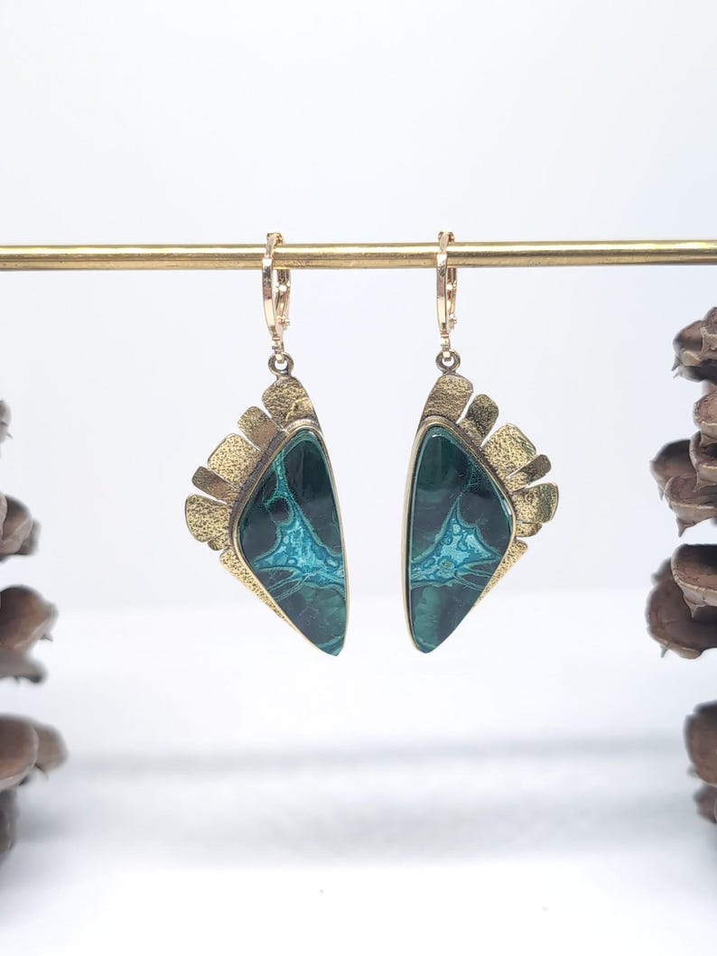 May include: A pair of drop earrings featuring triangular-shaped stones with deep green and bright turquoise marbled patterns. The stones are set in textured gold-tone metal frames with a fan-like edge and attached to small gold-tone hoop clasps.