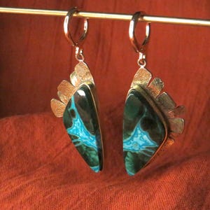 May include: A pair of dangle earrings featuring triangular stones with dark green and bright turquoise veining. The stones are set in textured silver-toned metal with a fan-like design at the top, suspended from silver-toned lever-back ear wires.