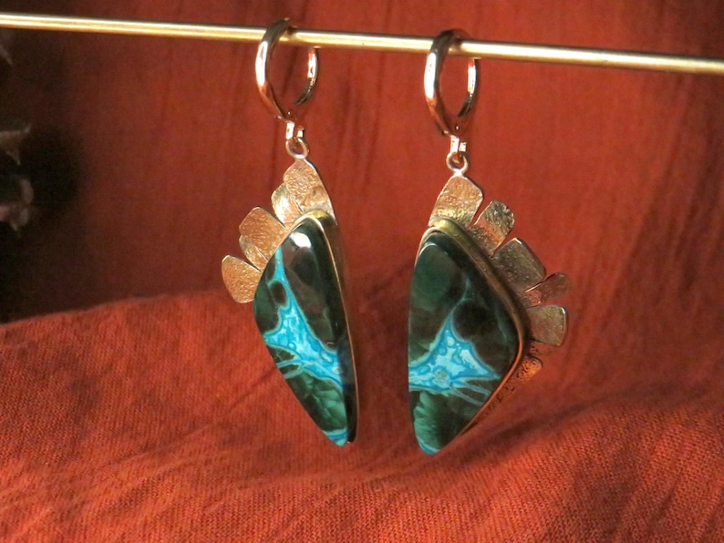May include: A pair of dangle earrings featuring triangular stones with dark green and bright turquoise veining. The stones are set in textured silver-toned metal with a fan-like design at the top, suspended from silver-toned lever-back ear wires.