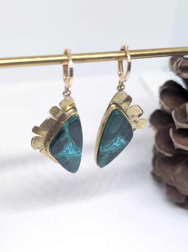 May include: A pair of dangle earrings featuring triangular dark green stones with intricate teal veining. Each stone is set in a textured gold-tone metal frame with a fan-like top edge, suspended from a small gold-tone hinged hoop earring component.