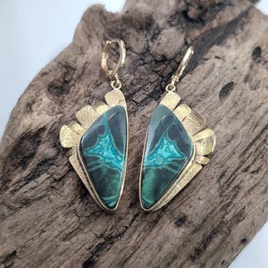 May include: A pair of drop earrings featuring triangular-shaped green and black patterned stones set in gold-toned metal. The metal settings have a textured, fan-like edge and include secure lever-back closures for attachment to the ear.