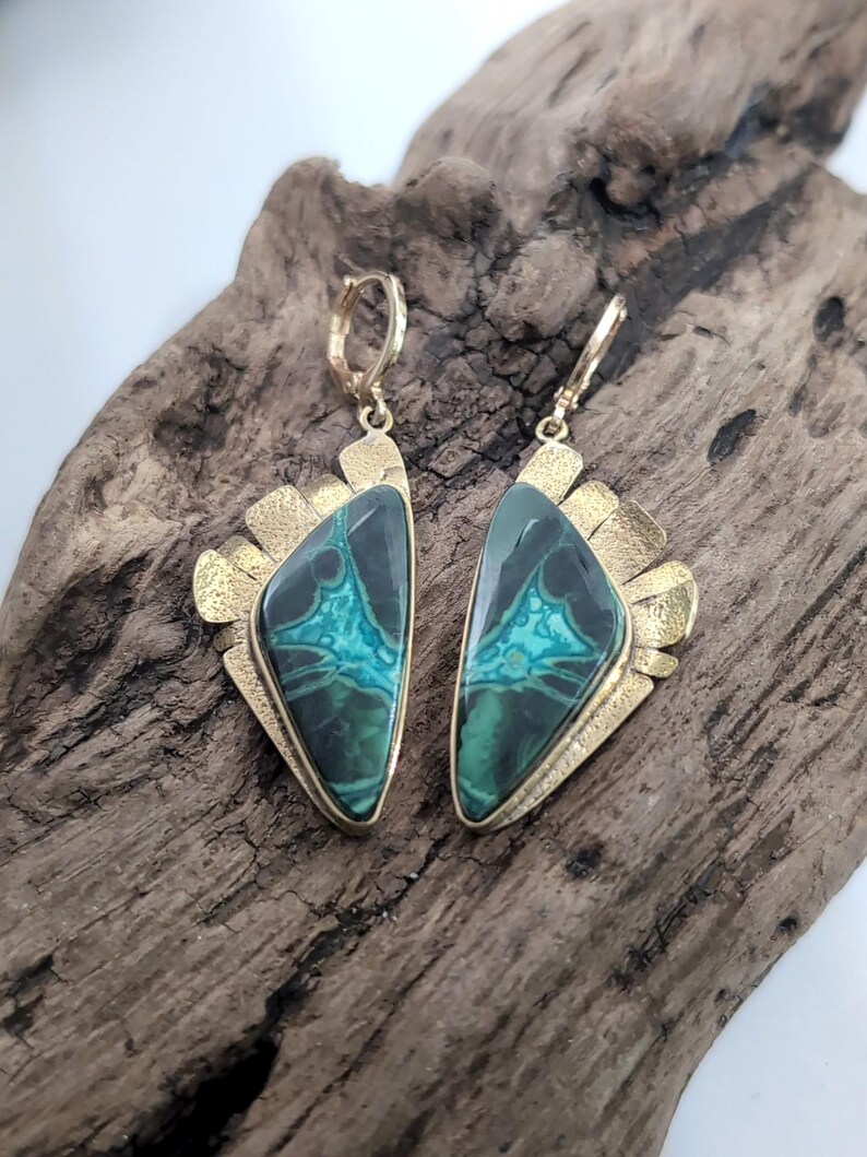 May include: A pair of drop earrings featuring triangular-shaped green and black patterned stones set in gold-toned metal. The metal settings have a textured, fan-like edge and include secure lever-back closures for attachment to the ear.