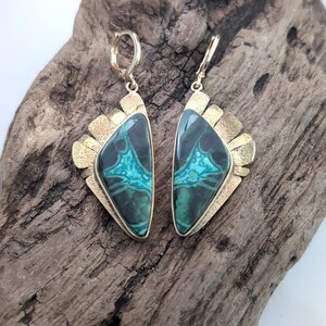 May include: A pair of dangle earrings featuring triangular stones with dark green and bright turquoise veining. The stones are set in textured gold-toned metal frames with a fan-like design along the top edge and secure lever-back closures.