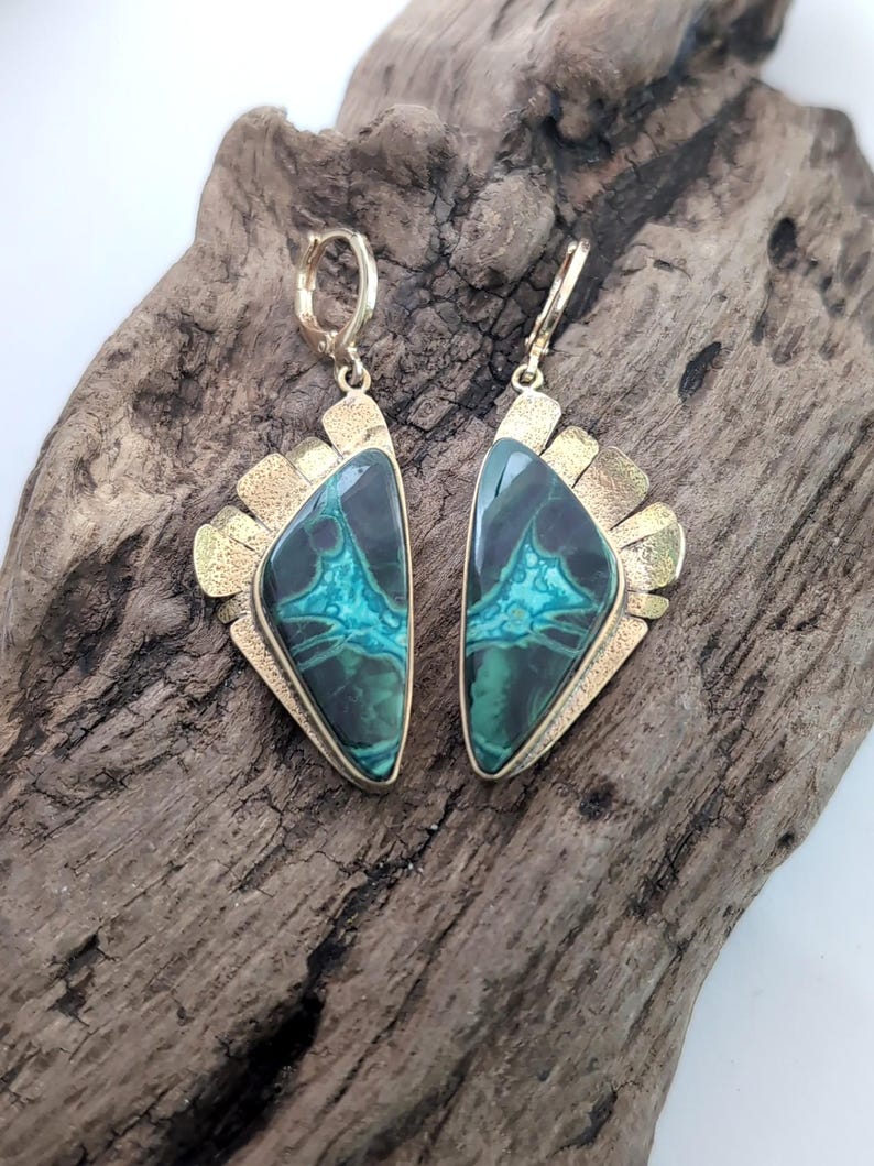 May include: A pair of dangle earrings featuring triangular stones with dark green and bright turquoise veining. The stones are set in textured gold-toned metal frames with a fan-like design along the top edge and secure lever-back closures.