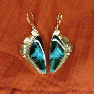 May include: A pair of dangle earrings featuring triangular-shaped stones with dark green and bright turquoise veined patterns. The stones are set in textured gold-tone metal frames with lever-back closures, creating a distinct geometric appearance.