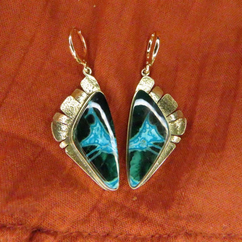 May include: A pair of dangle earrings featuring triangular-shaped stones with dark green and bright turquoise veined patterns. The stones are set in textured gold-tone metal frames with lever-back closures, creating a distinct geometric appearance.