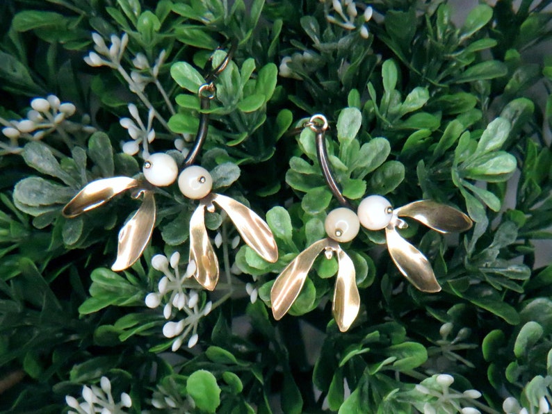 May include: A pair of gold-toned earrings with a delicate, leaf-like design and white pearl accents.