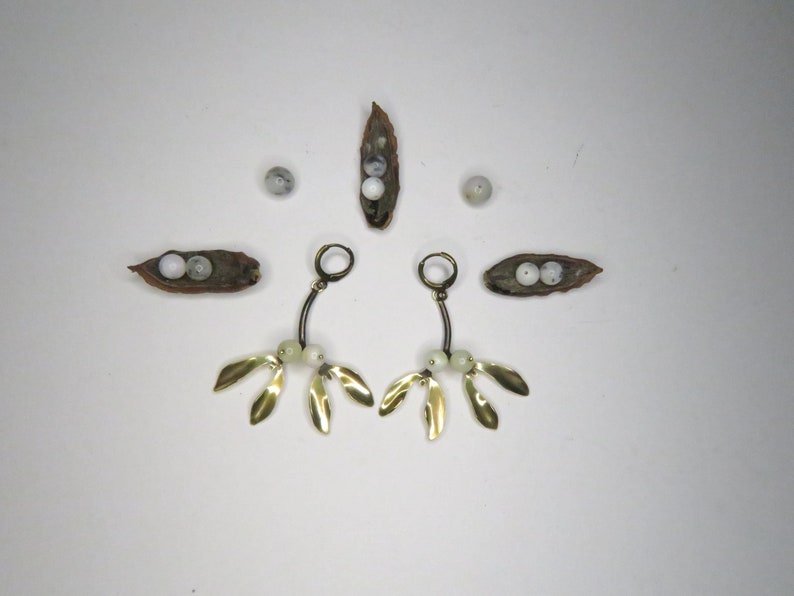 May include: A pair of gold earrings with white beads and gold leaf accents. The earrings are hanging from a hoop and have a delicate, organic design.