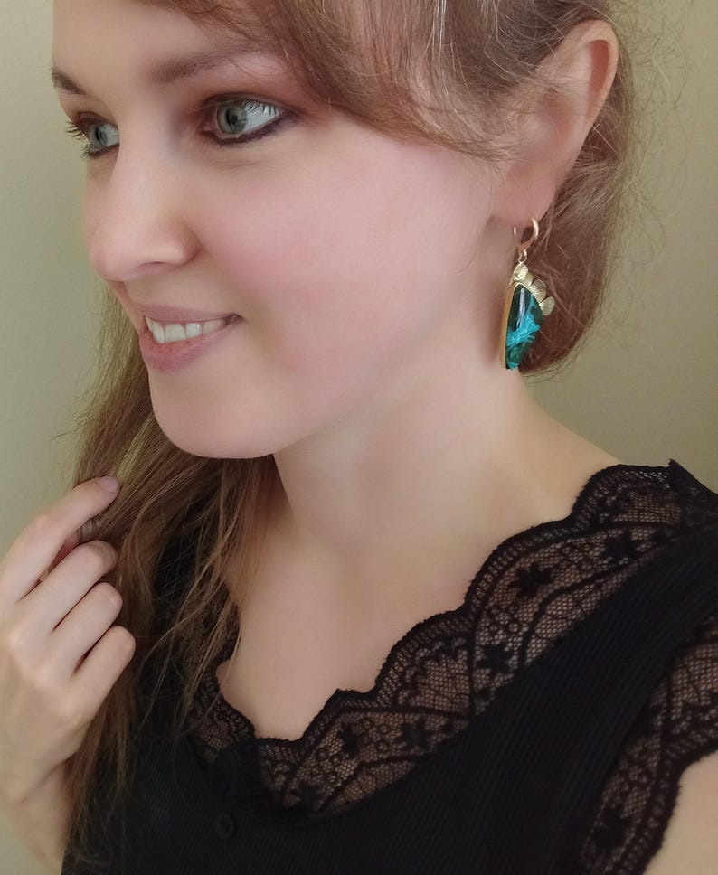 May include: A drop earring featuring a triangular-shaped piece with a vibrant teal and black marbled pattern, set in a gold-toned metal frame with a small decorative scalloped edge at the top, suspended from a simple gold-toned ear wire hook.