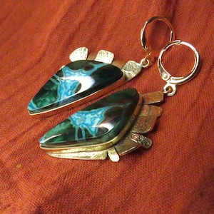 May include: A pair of dangle earrings featuring triangular stones with dark green and bright blue marbled patterns. The stones are set in textured gold-tone metal frames with a jagged edge design and attached to gold-tone leverback closures.