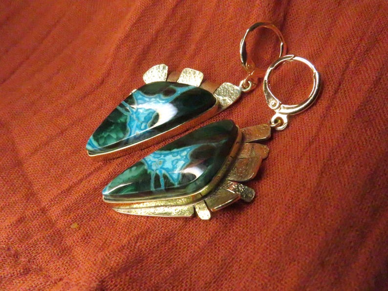 May include: A pair of dangle earrings featuring triangular stones with dark green and bright blue marbled patterns. The stones are set in textured gold-tone metal frames with a jagged edge design and attached to gold-tone leverback closures.