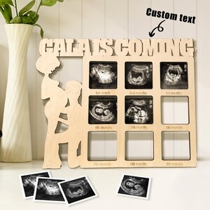 May include: Wooden pregnancy announcement frame with the text "CALAIS IS COMING". The frame has spaces for ultrasound photos labeled by month. A silhouette of a pregnant person and partner is on the left.