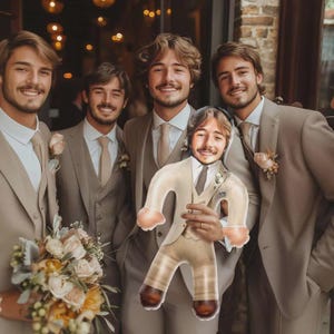 May include: A group of five men in tan suits, some holding a bouquet of flowers and a novelty inflatable doll resembling a man in a suit. The men are smiling, suggesting a celebratory event.