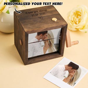 Puede incluir: Una caja de música de madera oscura con una foto de una pareja besándose. La caja tiene un pequeño botón dorado y una manivela de madera. El texto "I love you always 22.07.2025" está grabado en la parte superior. El texto "PERSONALIZED YOUR TEXT HERE!" está arriba.