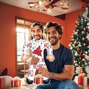 May include: A novelty Christmas-themed inflatable doll in the shape of a man, held by a person. The doll is white with red accents, including a Christmas tree design and the words "HO HO HO". The person is wearing a dark blue shirt.