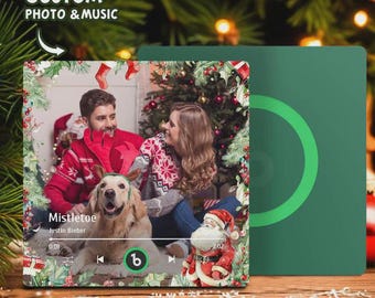 Pode incluir: Uma placa personalizada de foto e música com tema natalino com um casal e um cachorro. A placa tem uma borda festiva com azevinho e bagas. O texto "Mistletoe" e "Justin Bieber" são visíveis. Uma capa verde está à direita.