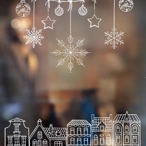 Può includere: Disegno a tratto bianco di ornamenti natalizi, fiocchi di neve e stelle appesi a una corda. Sotto, è raffigurata una fila di case stilizzate. Lo sfondo è una scena sfocata dai toni caldi, che suggerisce un'atmosfera festosa.