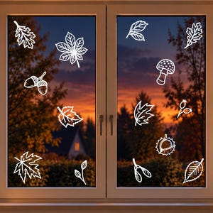 May include: A set of white line art window decals featuring various autumn-themed motifs including maple leaves, oak leaves, acorns, a mushroom, berries, and a chestnut shell, applied to the glass panes of a double-casement window frame.