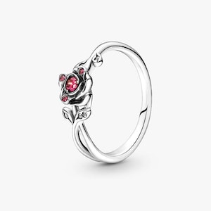 Puede incluir: Anillo de plata con diseño de rosa, con una gema roja central y pequeños acentos rojos. La banda del anillo tiene un diseño curvo, con detalles de hojas y piedras de acento transparentes.