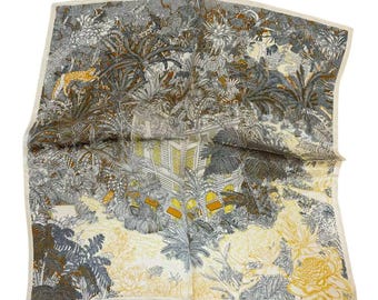 May include: A square silk scarf with a beige background and a colorful print of a jungle scene with a building in the center. The print features palm trees, flowers, and animals in shades of brown, yellow, and gray.