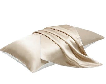 May include: A beige silk pillow with a white border, draped with a matching silk scarf. The pillow is rectangular and appears soft, with a subtle sheen. The scarf is folded over the pillow, adding a touch of elegance.