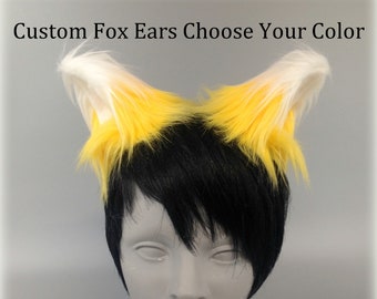 May include: Custom Fox Ears Choose Your Color. A pair of faux fur fox ears featuring a gradient of bright yellow at the base transitioning to white tips. The ears are attached to a black wig worn on a grey mannequin head. The fur is long and textured.