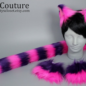 May include: A pink and purple cat tail, a pair of pink and purple paw cuffs, and a pink and purple cat ear headband. The headband is worn on a mannequin head with black hair.