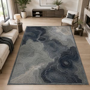 Könnte beinhalten: Ein rechteckiger Teppich mit einem abstrakten, fließenden Muster in tiefem Marineblau, Anthrazit und hellem Silber. Das Design ahmt organische, geschichtete geologische Formationen mit wirbelnden, marmorierten Linien auf der gesamten Oberfläche nach.