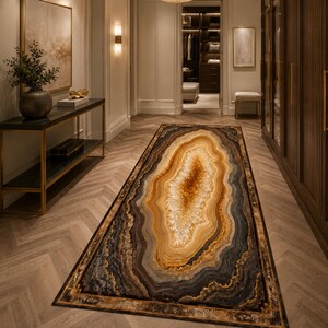 Può includere: Un tappeto rettangolare con un design a pietra d'agata. Il tappeto presenta un motivo centrale di toni marrone caldo, oro e crema, circondato da fasce di grigio, nero e marrone scuro. Il tappeto è bordato da un bordo dorato.