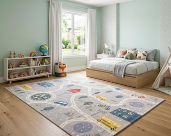 May include: A rectangular area rug featuring a light gray background with a printed road map design. The pattern includes yellow school buses, blue buildings, trees, bicycles, and circular motifs. The rug is placed on a light wood floor in a room.