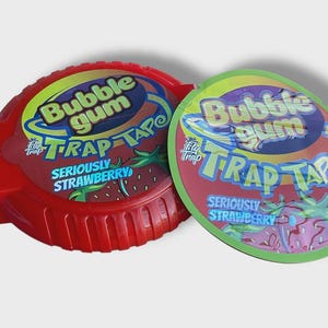 May include: Two containers of bubble gum. One is red and the other is green. Both have the words "Bubble Gum Trap Tape" and "Seriously Strawberry" printed on them. The bubble gum containers are round.