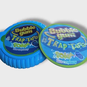 May include: Two blue bubble gum containers. One is a dispenser, the other a lid. Both have the text "Bubble Gum Trap Tape Sour Blue Raspberry" in a colorful design. The dispenser is a bright blue color.