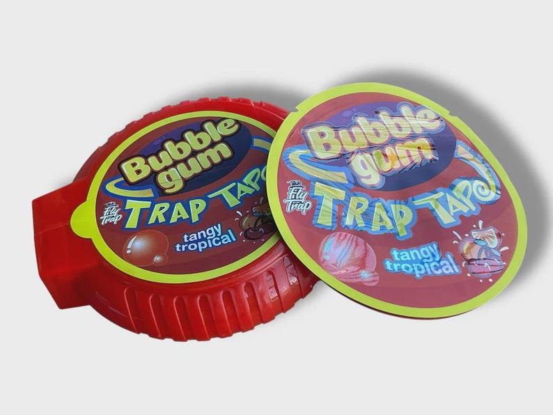 May include: Two containers of Bubble Gum Trap Tape, a tangy tropical bubble gum. The red container is oval-shaped with a ridged edge. The lid is a maroon color with yellow and blue text.