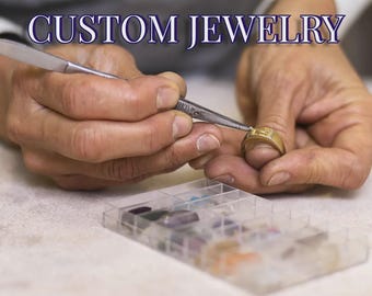 Puede incluir: Un anillo de oro siendo trabajado con pinzas de metal, con el texto CUSTOM JEWELRY en la parte superior. Una caja organizadora de plástico transparente que contiene varias piedras preciosas pequeñas y coloridas está en primer plano.