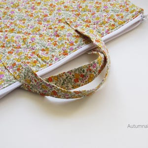 May include: A floral quilted bag with a white zip and handle. The bag features a pattern of yellow, orange, and pink flowers on a light background. The text "Autumnal floral" is visible.